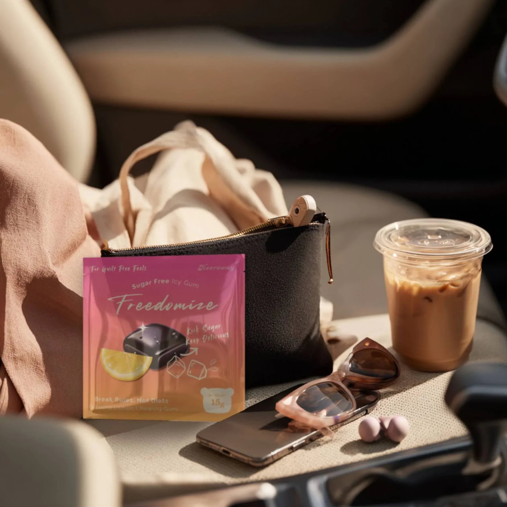 A Freedomize bursting lemon Sugar Free Icy Gum pouch placed on a car seat next to sunglasses, iced coffee, and a tote bag.