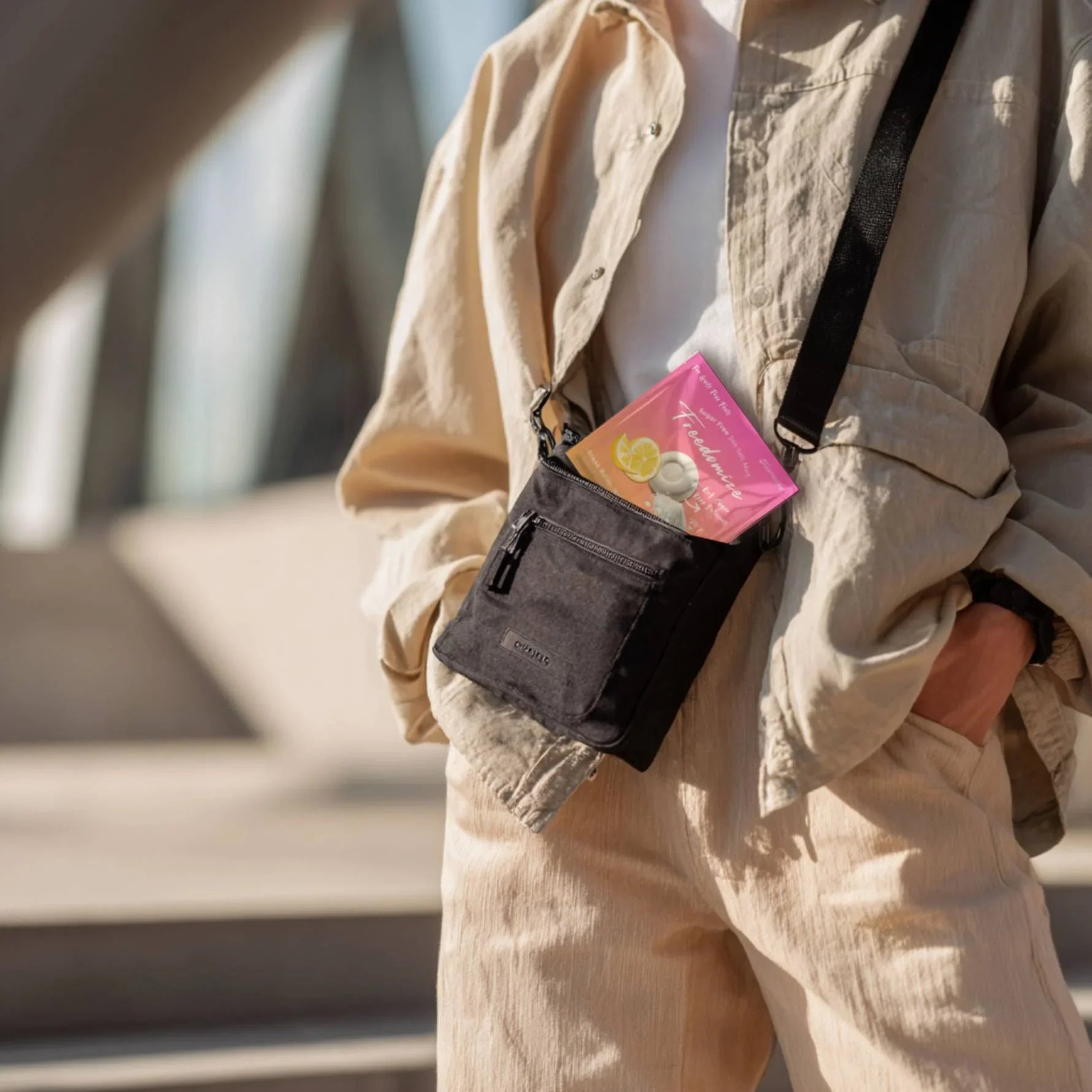 Person in beige outfit carrying a black crossbody bag with a visible pouch of Freedomize Salted Lemon Lime Chill Sugar-Free Sea Salt Mint tucked inside.