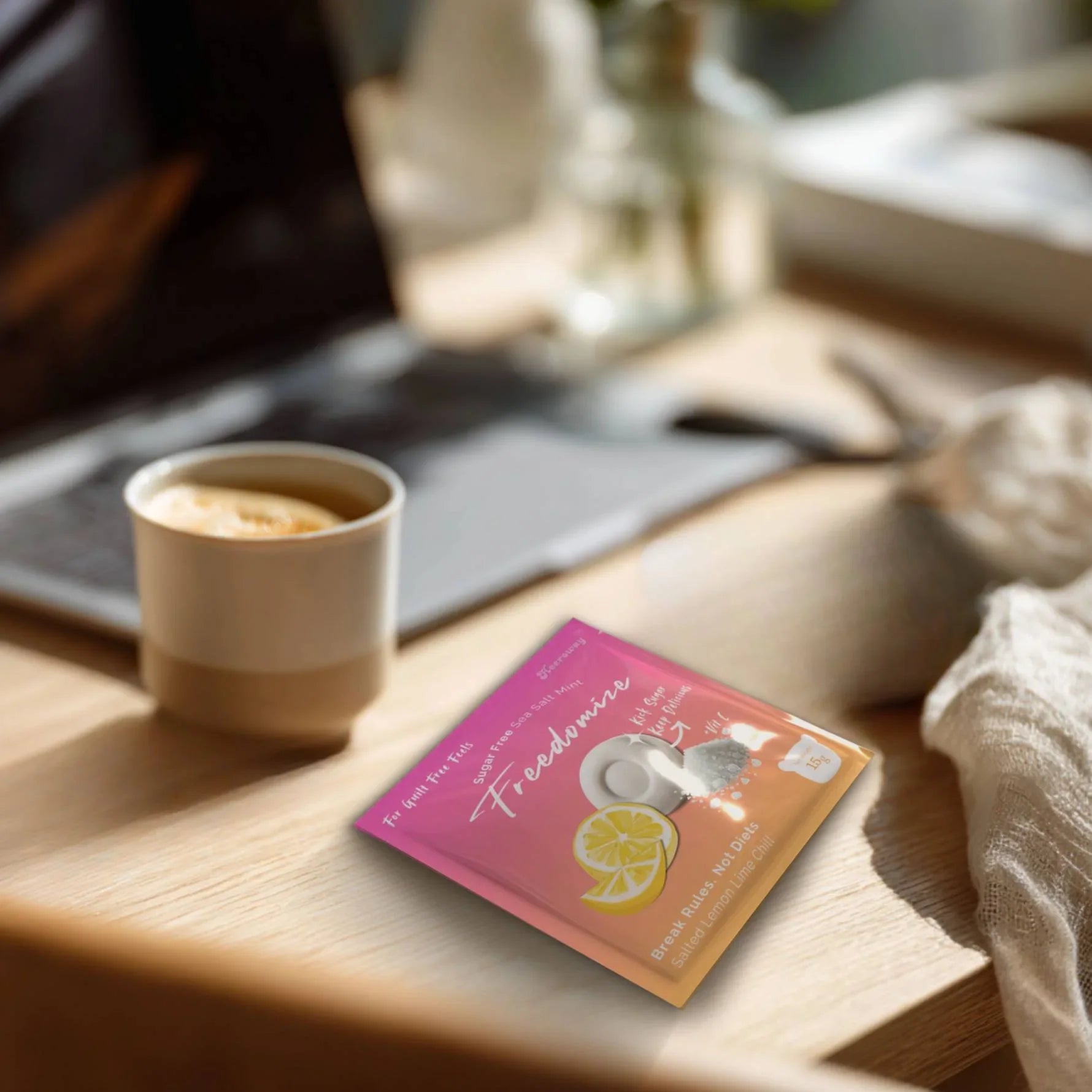 Freedomize Salted Lemon Lime Chill sugar-free sea salt mint pouch on a wooden desk beside a coffee cup and laptop, captured in natural light.