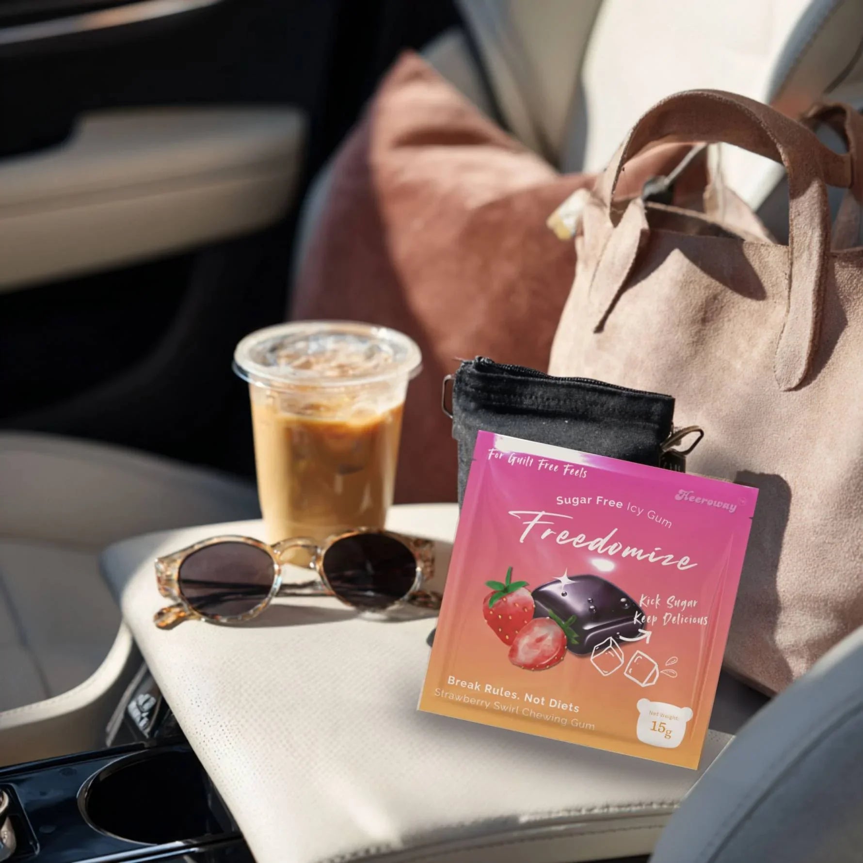 A Freedomize Strawberry Swirl Sugar Free Icy Gum pouch placed on a car seat next to sunglasses, iced coffee, and a tote bag.