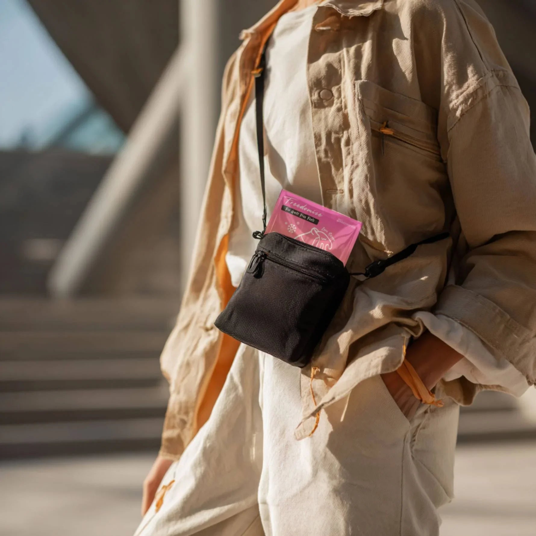 Person wearing a beige outfit with a crossbody bag holding a Freedomize cool cola blast sugar-Free Icy Mints pouch outdoors in product page.