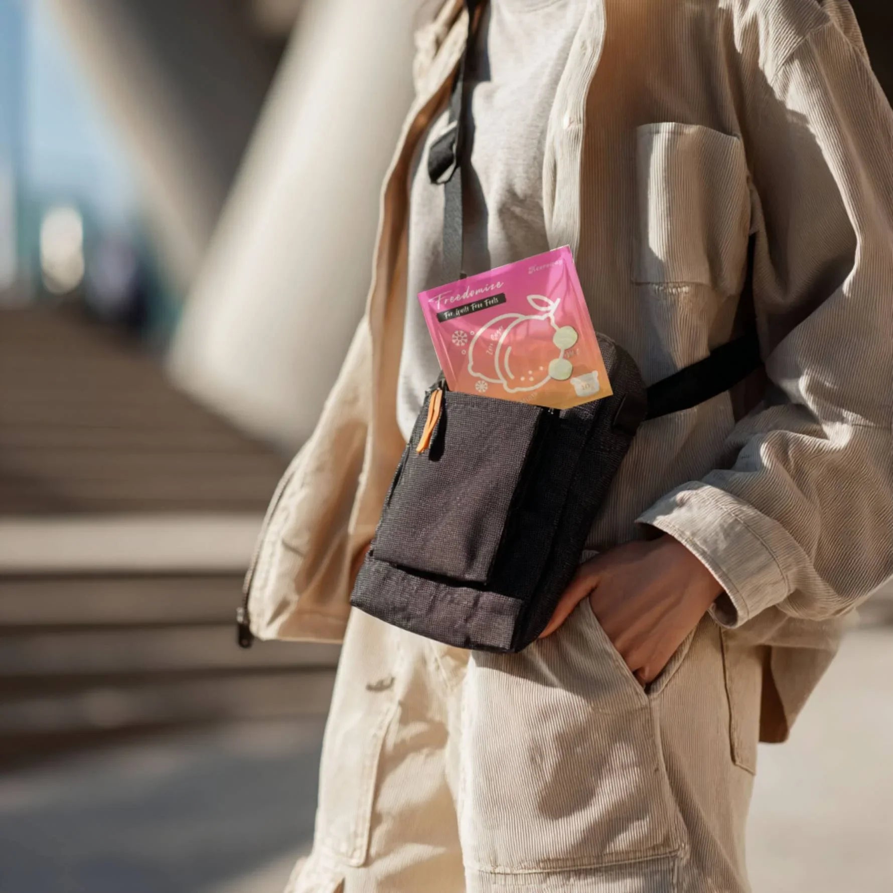 Person wearing a beige outfit with a crossbody bag holding a Freedomize Frosty Lemon Sugar-Free Icy Mints pouch outdoors in product page.