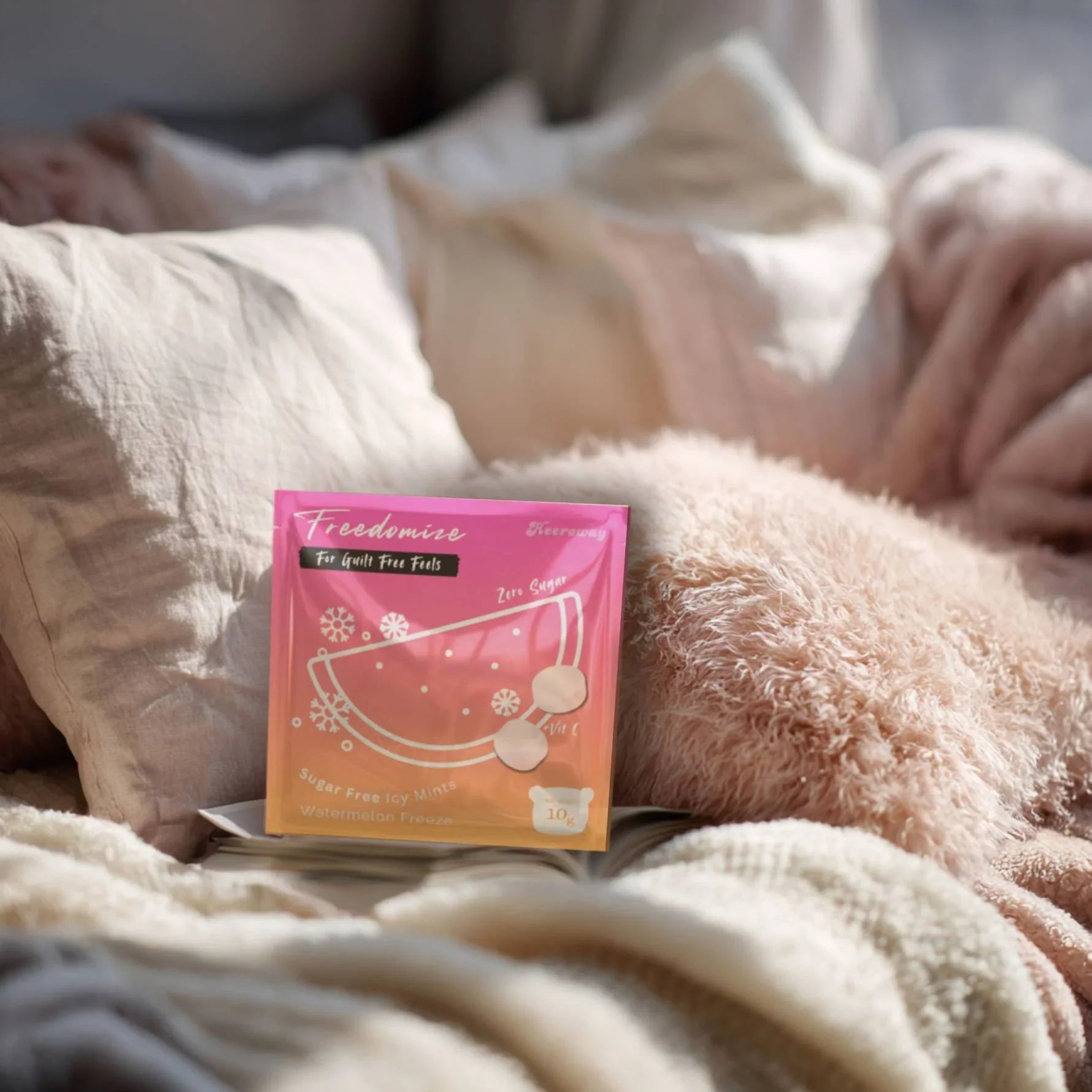 Freedomize Watermelon Freeze Sugar-Free Icy Mints pouch placed on a cozy bed with soft pink pillows, blanket, and a coffee cup nearby for icy mint variety bundle product page.