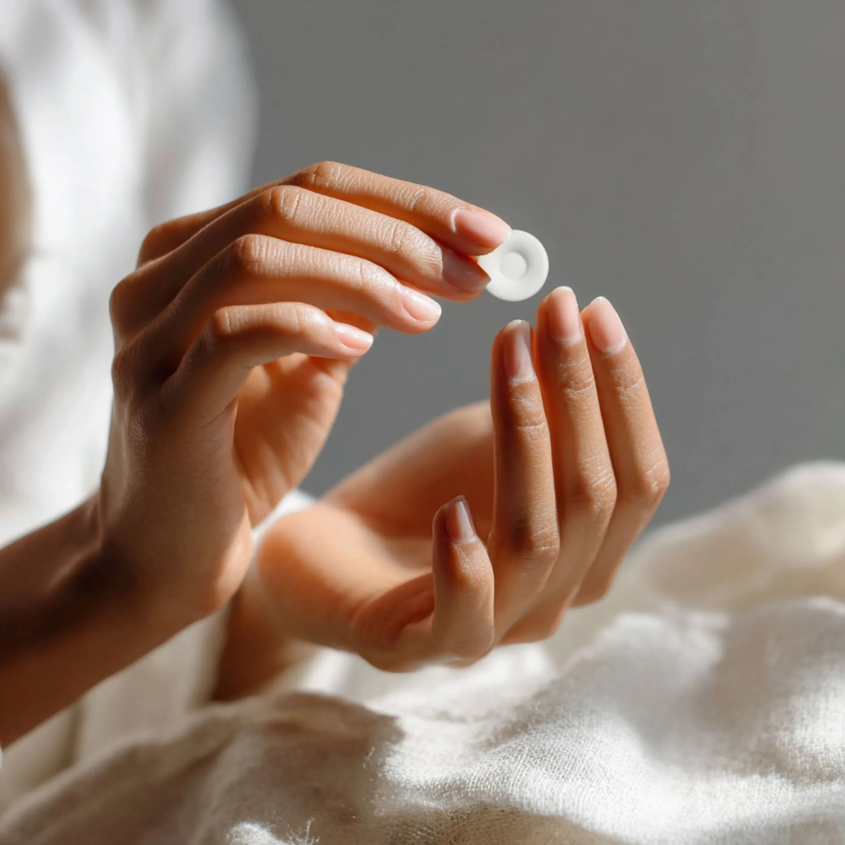 Close-up of hands holding a white round Heeroway Sea Salt Mint Lemon candy against a soft fabric background.