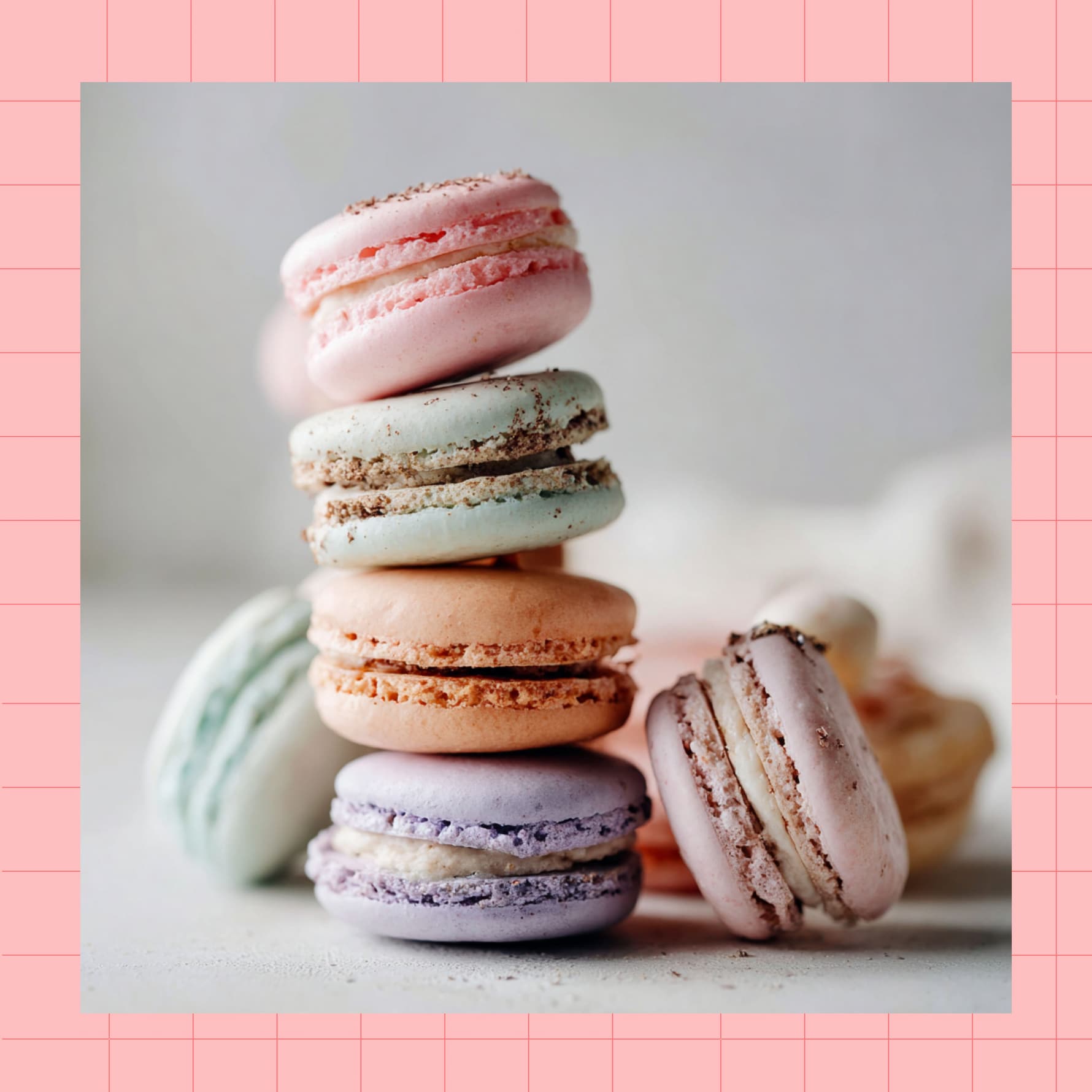 A stack of colorful pastel macarons in pink, blue, orange, and purple shades against a soft background with a pink grid border