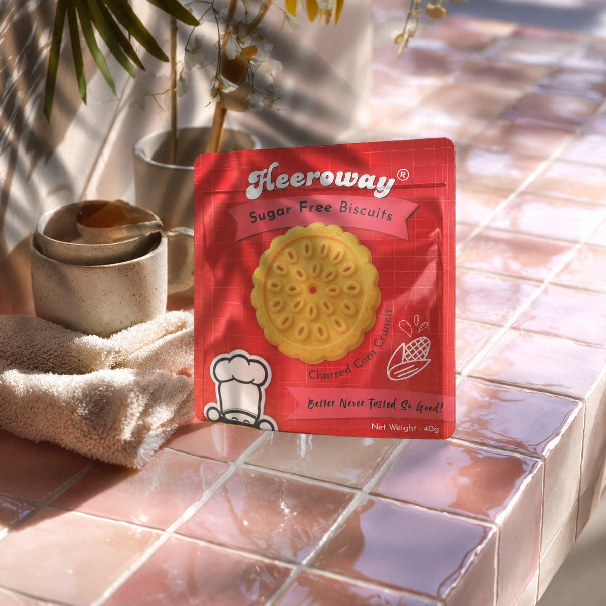 A packet of Heeroway Sugar Free Charred Corn Biscuits stands on a pink tiled surface with warm sunlight and shadows in a sunny afternoon.