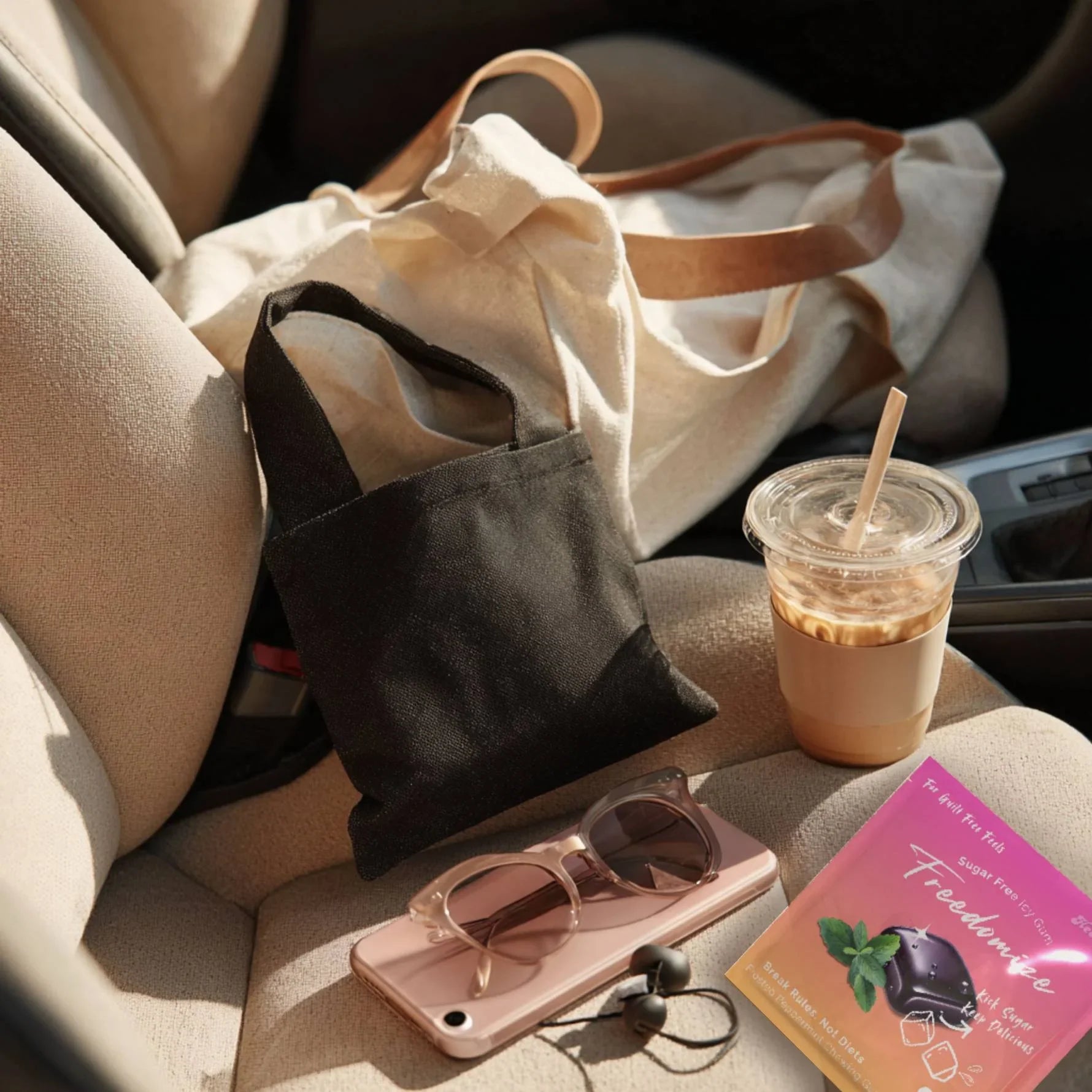 A Freedomize frosted peppermint Sugar Free Icy Gum pouch placed on a car seat next to sunglasses, iced coffee, and a tote bag.