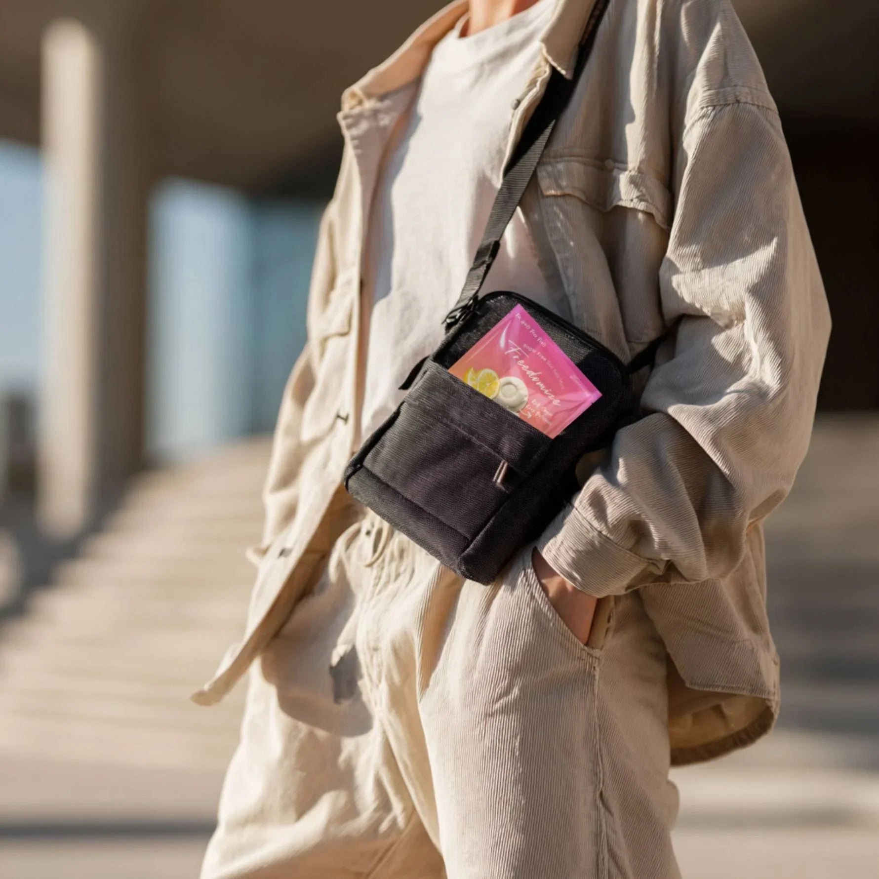 Person in beige outfit carrying a black crossbody bag with a visible pouch of Freedomize Salted Pineapple Chill Sugar-Free Sea Salt Mint tucked inside.