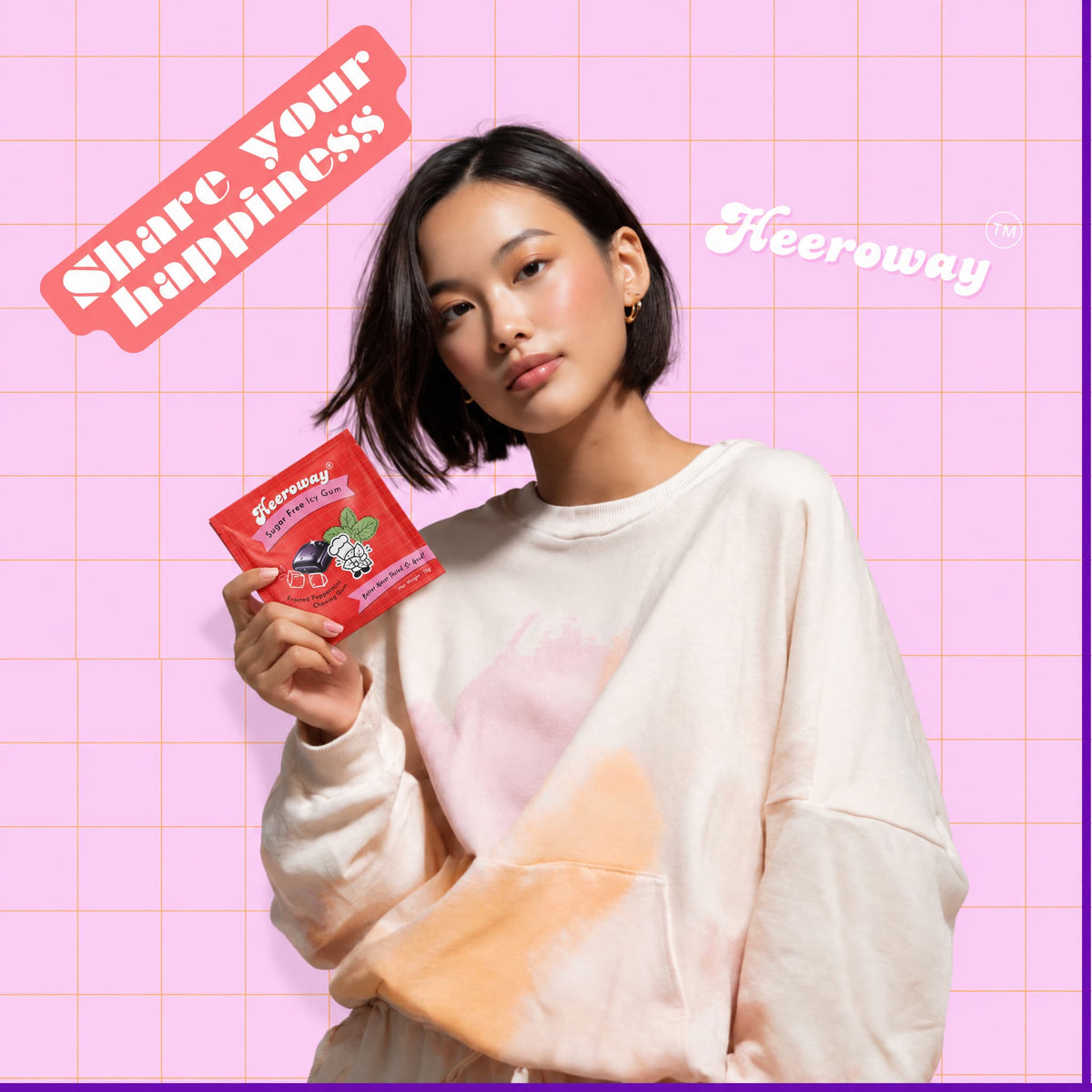 A woman with short dark hair holds a red packet of Heeroway strawberry chewing gum . She is wearing a cream-colored sweatshirt with pink and orange tie-dye patterns for icy mint bundle pack page.