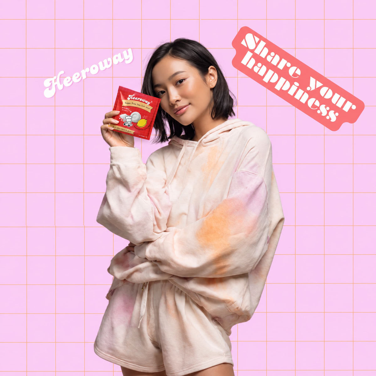 Young woman holding Heeroway  Sea Salt Mint pouch against a pink grid background. Main banner image for Heeroway Snacks product page.
