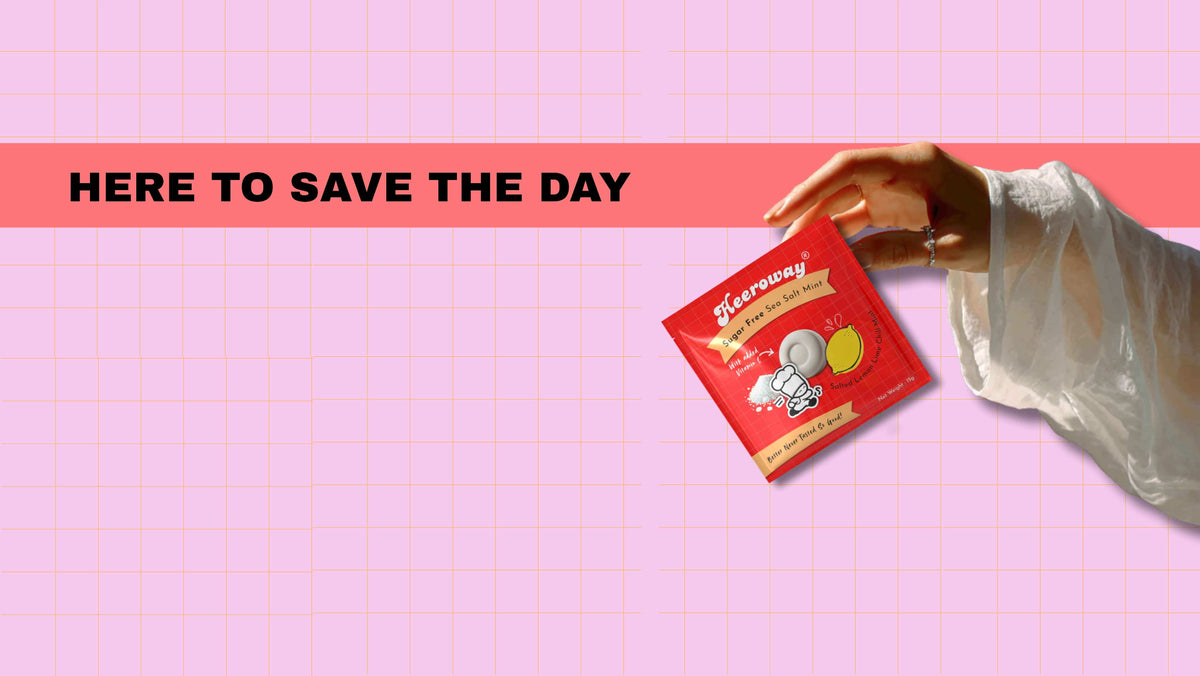 hand holding Heeroway sea salt mint sugar free packaging with lemon and mint design on pink grid background and text here to save the day