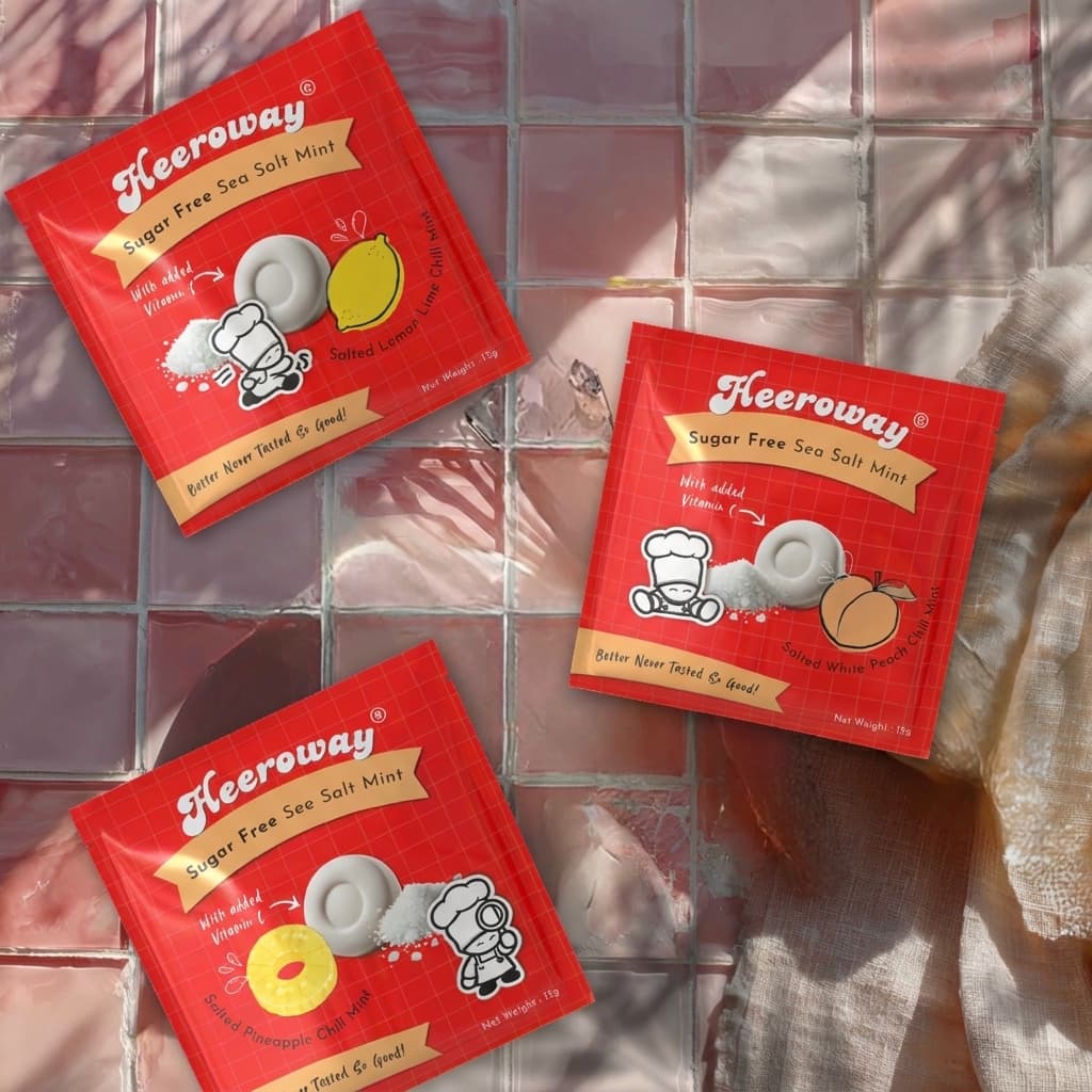 Three packets of Heeroway Sugar Free Sea Salt Mint pouch arranged on a pink-tiled surface with a beige cloth in the corner.