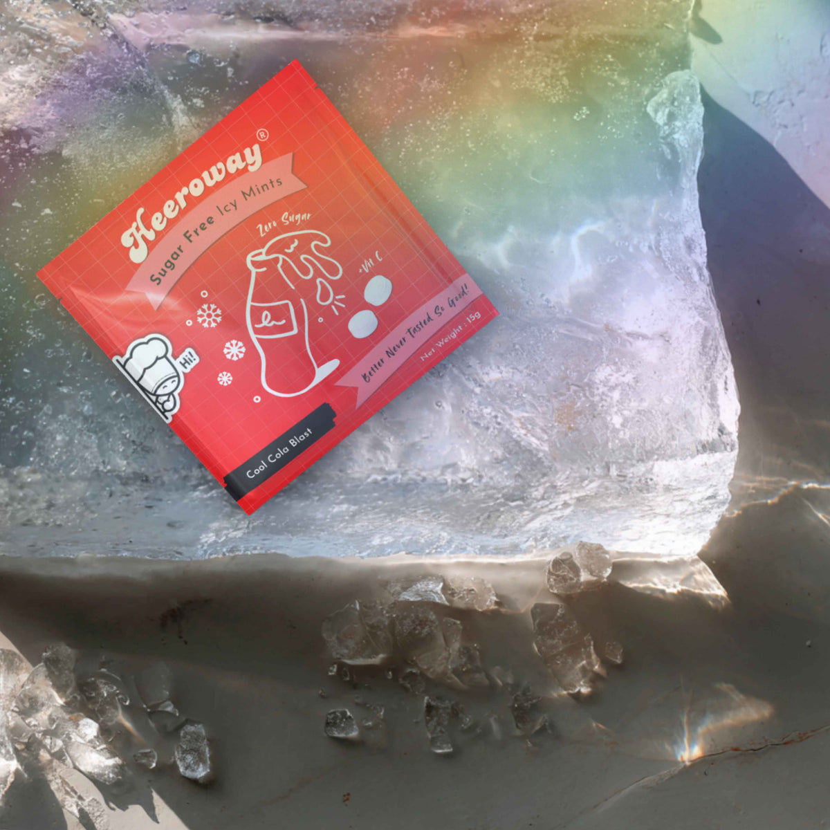 A packet of Heeroway Sugar Free Cola mint  candy is placed on a large block of ice with scattered ice crystals on a gray stone surface.