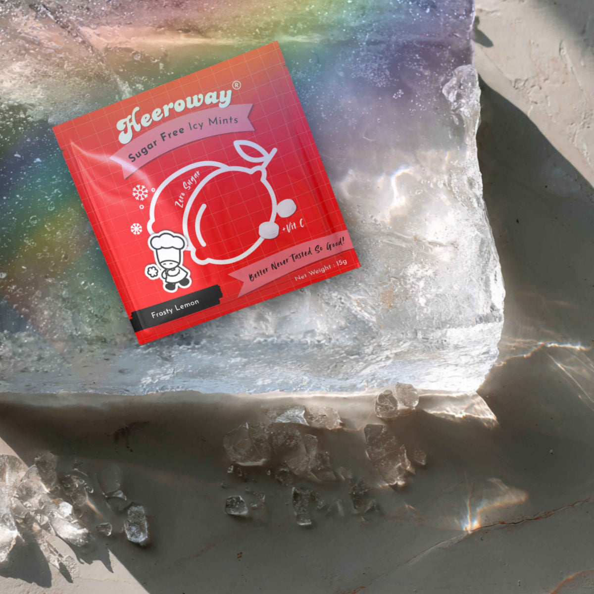A red packet of Heeroway frosty lemon mint resting on a large piece of ice, with scattered ice chunks on a gray surface.