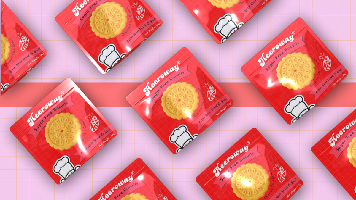 Multiple packets of Heeroway sugar-free corn biscuit arranged diagonally on a pink grid background.