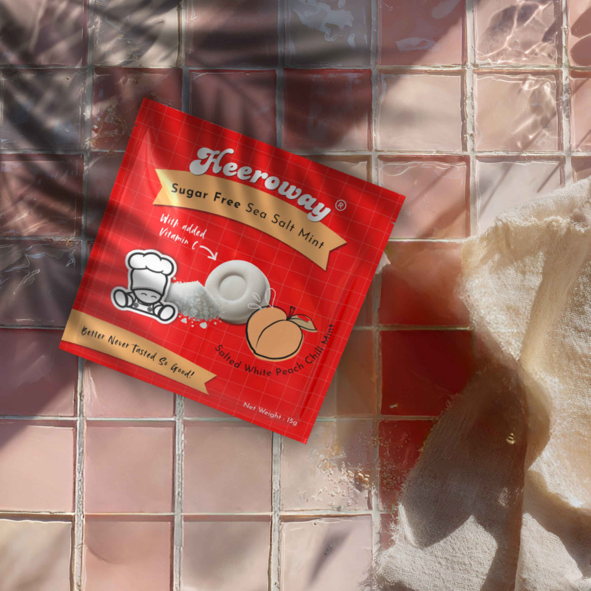 A packet of Heeroway Sugar Free Sea Salt Mint peach flavor  lies on a tiled surface with warm sunlight and shadows, next to a textured white cloth.
